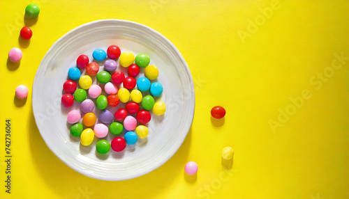 Multicolored candies on plate on yellow background. International No Diet Day is celebrated on May 6.Copy space.Pastel color.