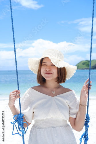 Woman in white dress and hat swinging on tropical beach, sunny day, good weather on lombok beach