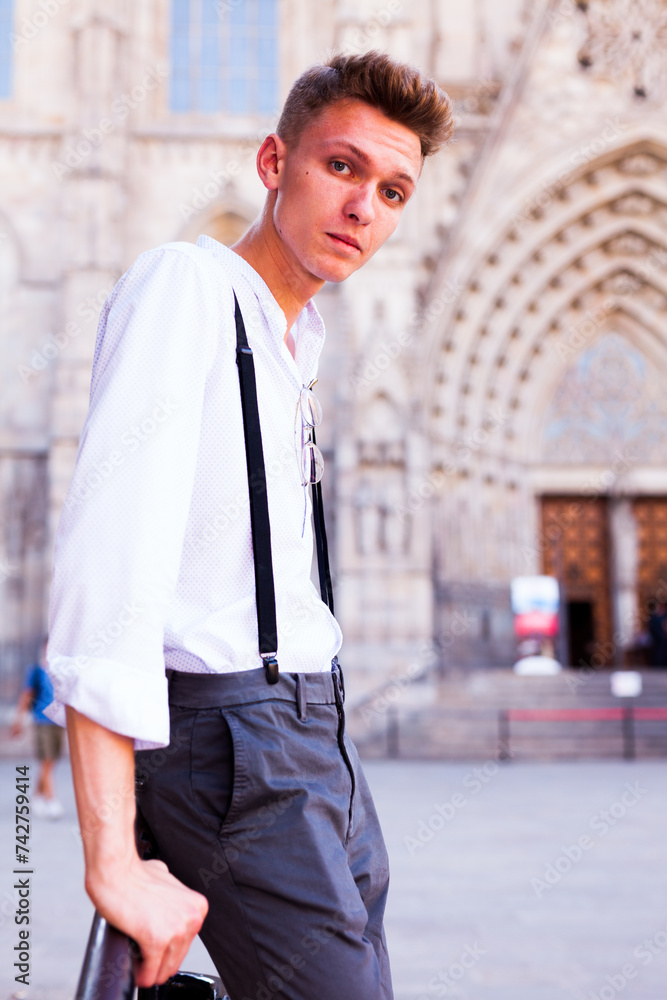 Young European guy in shirt and trousers with suspenders walking around city Young European guy in shirt and trousers with suspenders walking around city