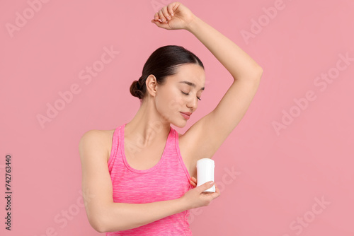 Beautiful woman applying deodorant on pink background