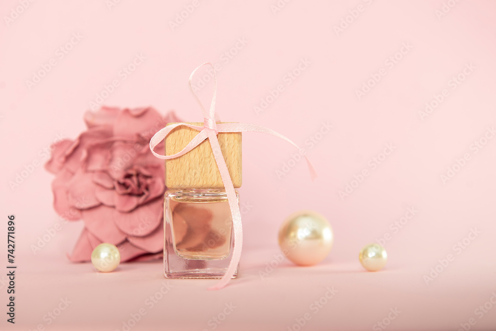 Perfume bottle with festive ribbon with camellia flower in peach fuzz color. Gift card for Mother's Day, Women's Day. Presentation of cosmetics as a gift.spring background, flat lay