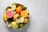 Different fresh citrus fruits and leaves in bowl on light table, top view. Space for text
