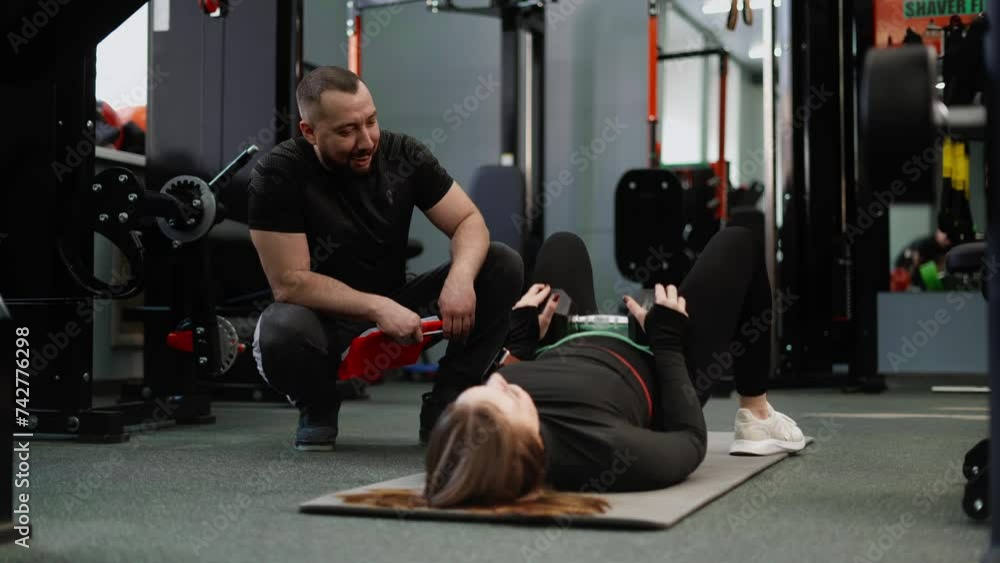 The trainer monitors and helps to perform the buttock reduction exercise correctly. Classes with an experienced coach in a gym with special equipment. The trainer monitors and helps to perform the buttock reduction exercise correctly. Classes with an experienced coach in a gym with special equipment.
