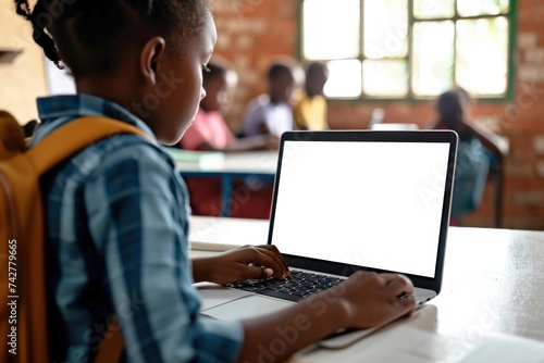 African junior school kid girl student using laptop computer with white blank empty mockup screen at desk in classroom. Online education class software website tech ads concept. Generative AI