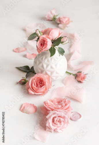 Light pink roses in a vase, petals and buds on white table close up, romantic and wedding
