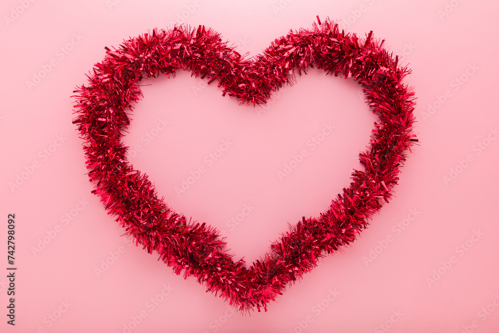 Big beautiful shiny red tinsel heart shape on light pink table background. Pastel color. Love concept. Closeup. Empty place for text in middle. Top down view.