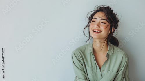 Asian woman wearing green shirt smiling laugh out loud isolated on grey © pariketan