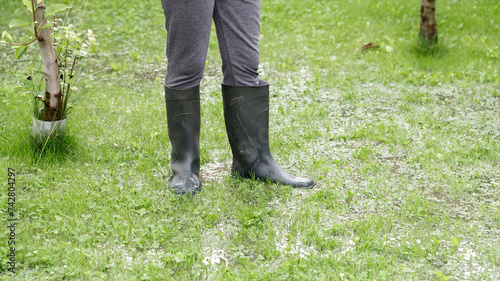 The person stands in the garden in the water, legs in wellies. The garden is flooded. Consequences of downpour, flood
