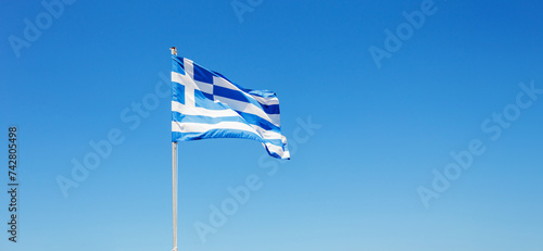 Greek flag waving proudly against a clear blue sky.