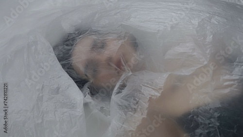 Female in underwear laying on the bed in the studio. Young woman seminude in lingerie laying posing under thin sheet of oilcloth wrap.