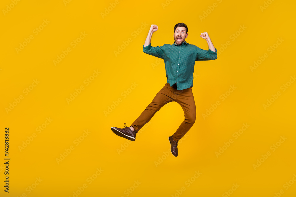 Full size photo of satisfied guy dressed dotted shirt brown pants fly win bet fists up screaming isolated on yellow color background