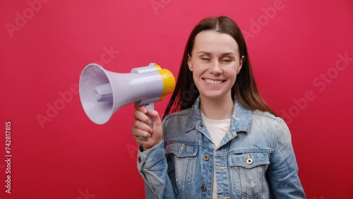 Portrait of surprised fun promoter young woman 25 old years wearing denim jacket scream in megaphone announces discounts sale Hurry up, posing isolated over plain red color background wall in studio