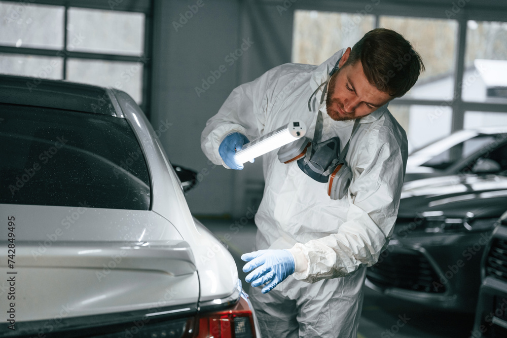 Rear part of automobile. Garage worker is holding lighting and checking surface of the car Rear part of automobile. Garage worker is holding lighting and checking surface of the car