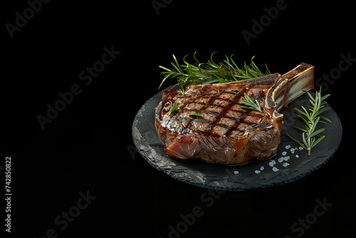 A grilled tomahawk steak on slate plate with salt and rosemary. Ribeye steak. Black color background, side view. Space for text.