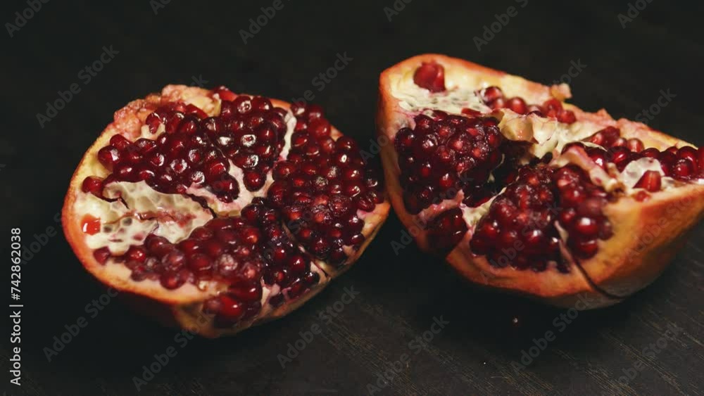 Ripe pomegranate opened in half on the black wooden table. Close up. Ripe pomegranate opened in half on the black wooden table. Close up.