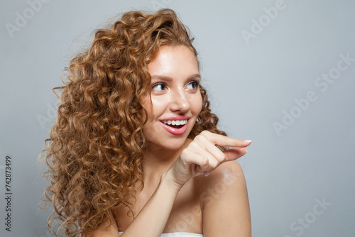 Happy woman pointing finger. Beautiful female model with natural make-up, frizzy long hair and friendly smile on white background