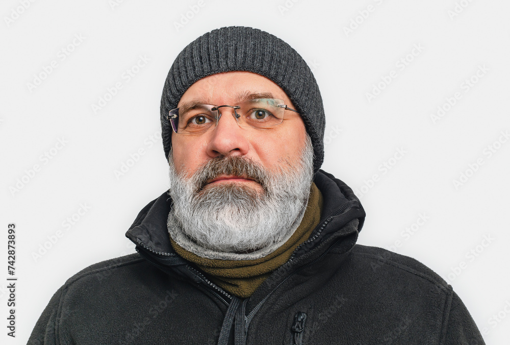 Serious man with gray beard and mustache in winter hat. Looks into camera. White background. Serious man with gray beard and mustache in winter hat. Looks into camera. White background.