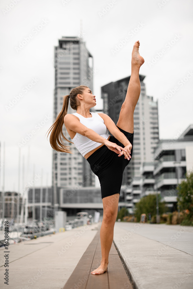 Young woman standing with leg raised high and arms outstretched