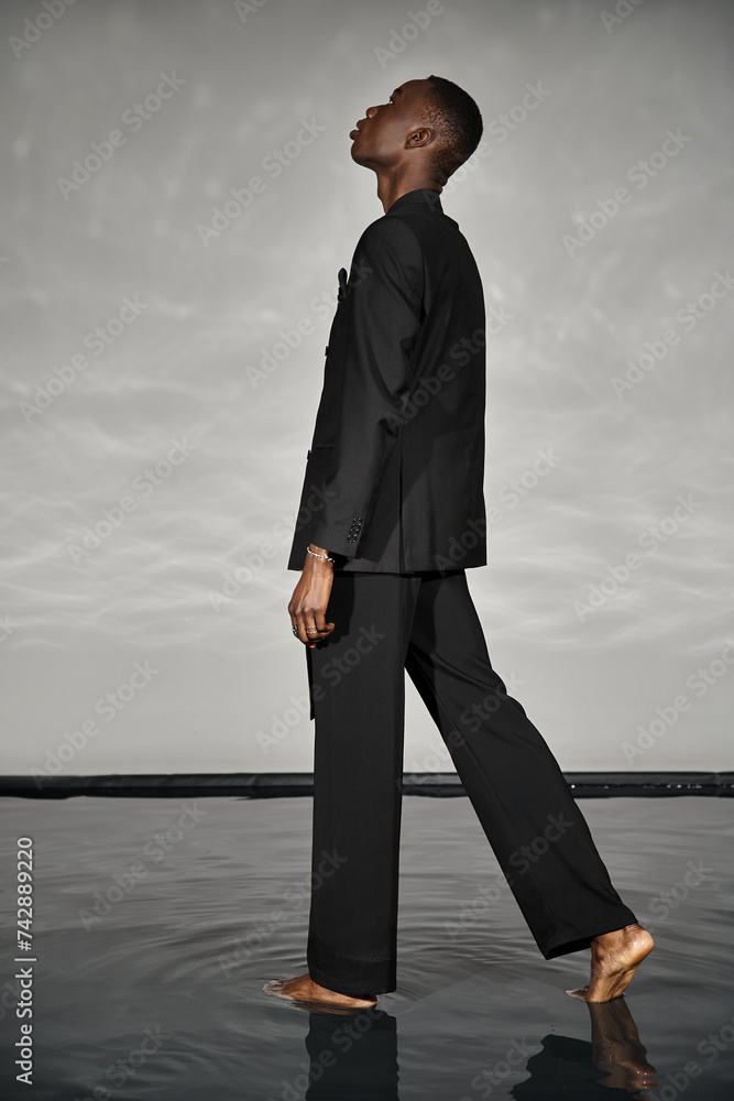 charming stylish african american man in sexy unbuttoned suit posing on gray watery background