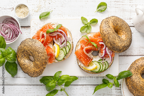Salmon sandwiches with bagel, salted fish, fresh cucumber, onion and basil on white background, top view. Healthy breakfast with salmon toasts photo