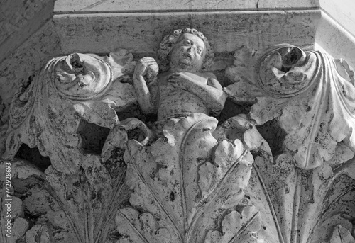 Venice, Italy, Sept. 17, 2023: A Doge’s Palace portico sculpture of a boy, or putto, amid ornate leaves, fruit in hand, shows the skill of the city’s medieval stone carvers. photo