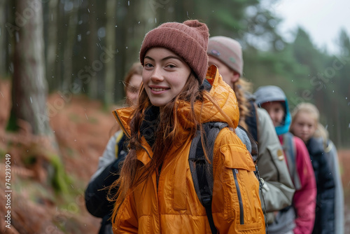 In the midst of a wintry forest  a group of hikers stand together  their smiling faces peeking out from behind warm scarves and jackets as they brave the rain and admire the towering trees against th