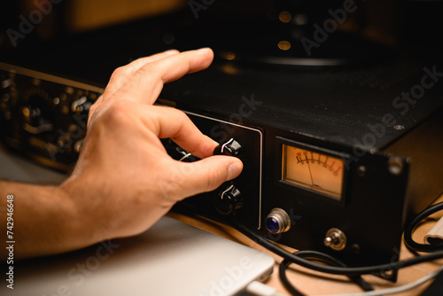 Close-up of a man's hand carefully turning a knob on a microphone preamplifier photo