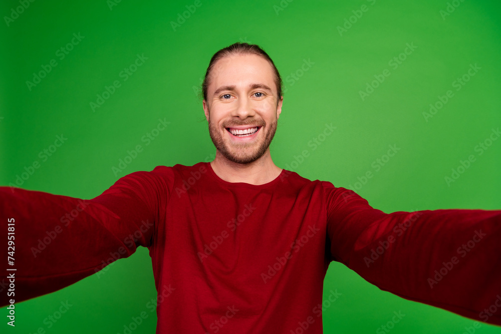Fototapeta premium Portrait of toothy beaming handsome guy with long hairstyle wear red sweatshirt smile on selfie isolated on green color background