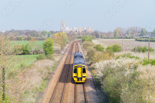 Railway train flanked by fields and ancient minster on horizon under blue sky. Beverley, UK.
