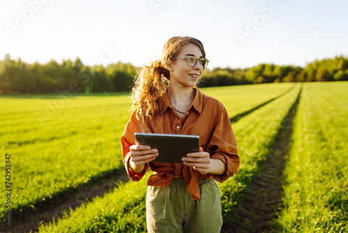 A woman farmer with a modern tablet in green field. Innovative smart farm system technology, agricultural management.