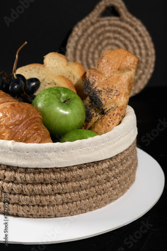 knitted jute basket with fruits and pastries on a dark background