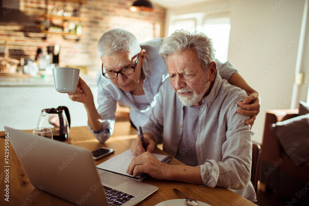 Senior man and woman reviewing documents and using laptop at home Senior man and woman reviewing documents and using laptop at home