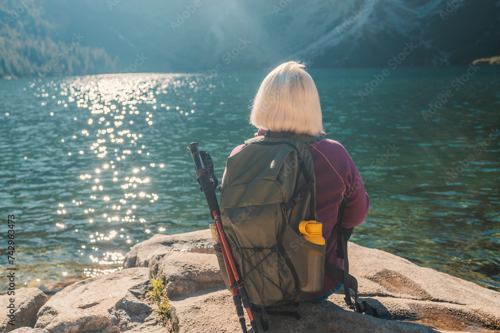 Lady tourist with a backpack standing on top of the mountain and enjoy the beautiful view of mountains Morskie Oko lake. Hiking travel and adventure in Poland, Tatry  - obrazy, fototapety, plakaty 