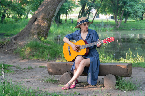 a woman in a blue dress and hat plays the guitar, a man in shorts shows how to play the guitar correctly