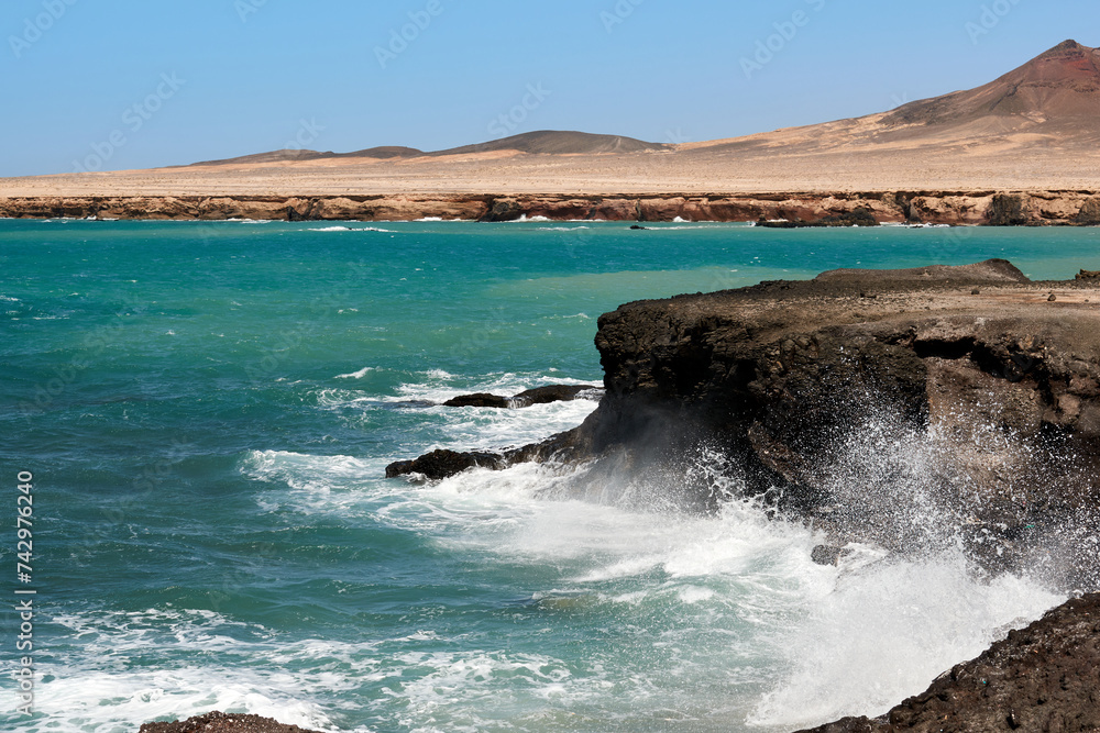 The Atlantic Ocean in Jandia with clear sky and mountains in the back and waves breaking on the shore