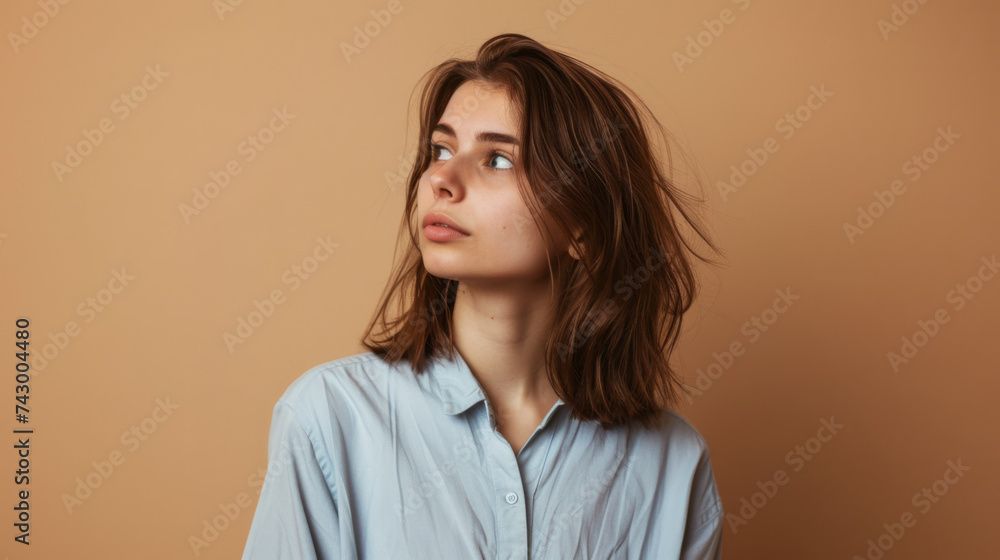 A young woman with shoulder-length hair gazes to the side against a neutral beige background, wearing a light blue shirt. A young woman with shoulder-length hair gazes to the side against a neutral beige background, wearing a light blue shirt.