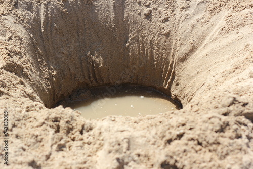 A deep hole dug in the beach sand on a bright sunny summer day.