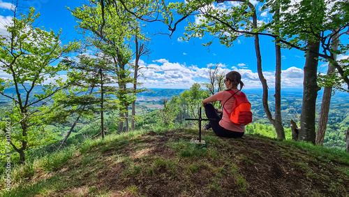Hiker woman at summit cross of Heiggerkogel in Grazer Bergland, Prealps East of the Mur, Styria, Austria. Scenic view of soft hill landscape. Idyllic hiking trail through lush green forest. Wanderlust