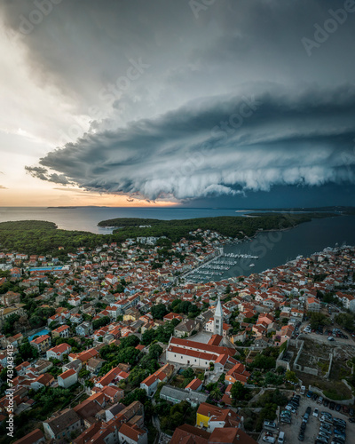 Aerial view of a menacing Supercell storm over a coastal town with red roofs and a church steeple, Mali Losinj, Primorje-Gorski Kotar, Croatia.