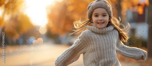 Active girl in warm sweater plays running in nature enjoying cool autumn air Little girl runs past village street on autumn day twilight Positive girl runs across countryside to bright sunset photo