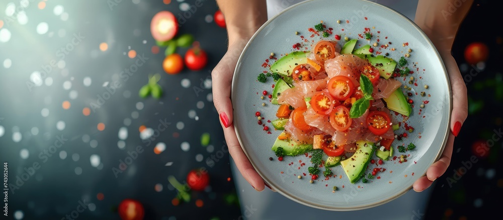 Crop unrecognizable female chef in apron standing with plate of delectable tartare made of fish with avocado and tomatoes. with copy space image. Place for adding text or design - obrazy, fototapety, plakaty 
