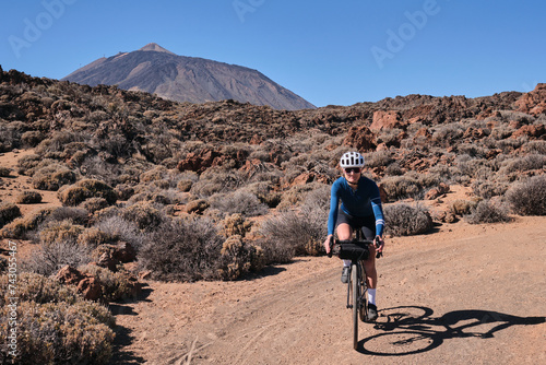 Woman cyclist practicing on gravel road. Female cyclist riding a gravel bike on gravel road with a view of the Teide volcano on Tenerife, Canary Island, Spain. Cycling gravel adventure. Effort mood.