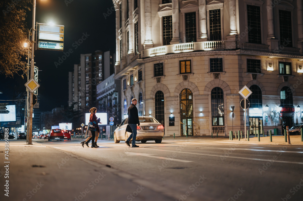 People crossing the street in a bustling city nighttime setting.