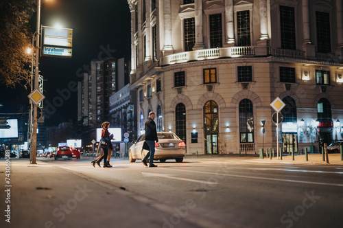 People crossing the street in a bustling city nighttime setting. © qunica.com