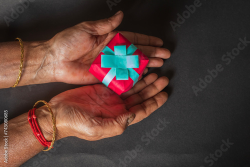 Wallpaper Mural Close up shot of Indian female hands holding a small gift box on a black background. Top view Torontodigital.ca