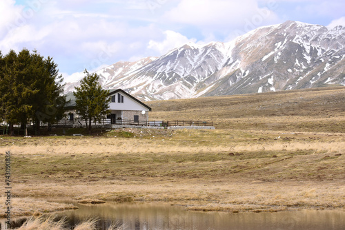baita o casa di montagna durante l'inverno con cime delle montagne innevate sullo sfondo e lago nella prateria photo