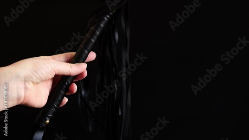 A woman's hand holds a whip against a dark background. Leather whip for spanking isolated on black. Sex toy for intimacy. Sexual slavery