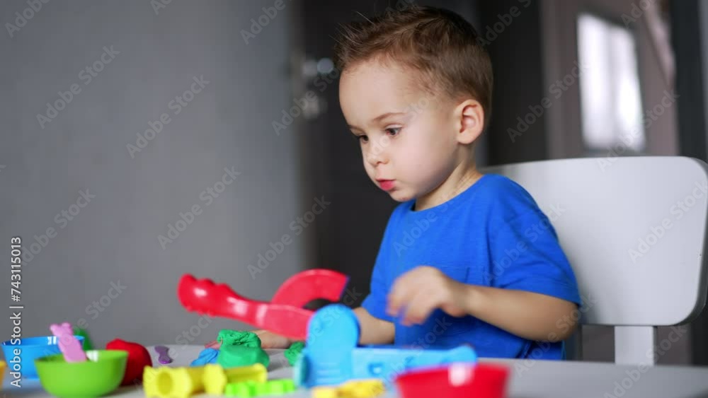 Concentrated Caucasian toddler sits at his desk at home. Cute baby boy sculpturing with plasticine. Concentrated Caucasian toddler sits at his desk at home. Cute baby boy sculpturing with plasticine.