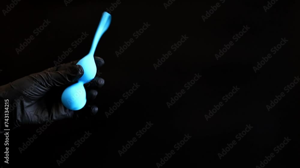 Hand in a black glove holds vaginal balls on a dark background. Blue vaginal balls in a woman's hand. Sex toys, sex shop concept Hand in a black glove holds vaginal balls on a dark background. Blue vaginal balls in a woman's hand. Sex toys, sex shop concept