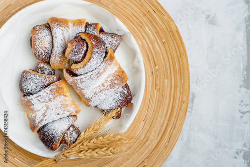 Croissants sprinkled with powdered sugar on a plate with spikelets on a light background. Top view, horizontal. Bakery products, pastries.